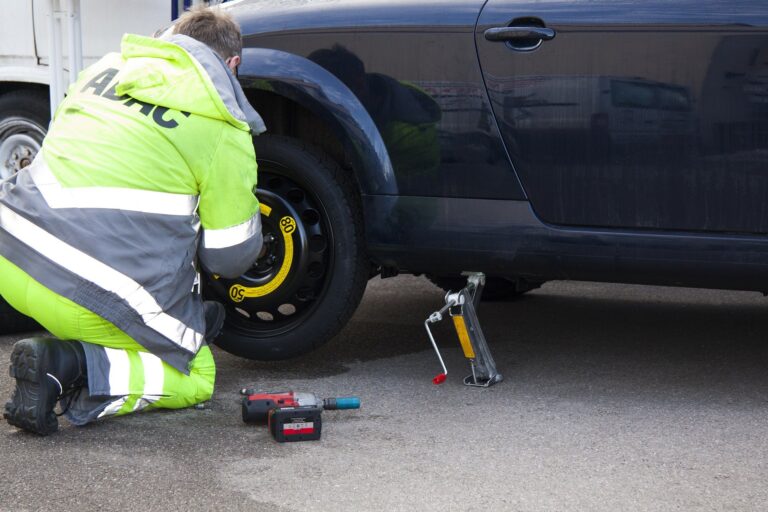 A man in a bright yellow jacket is fixing a flat tire on a vehicle