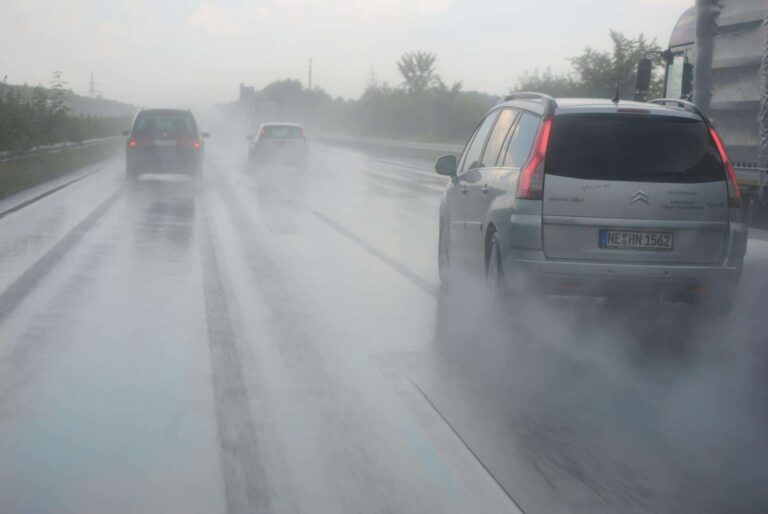 A car drives along a wet road, splashing water as it moves through the rainy weather